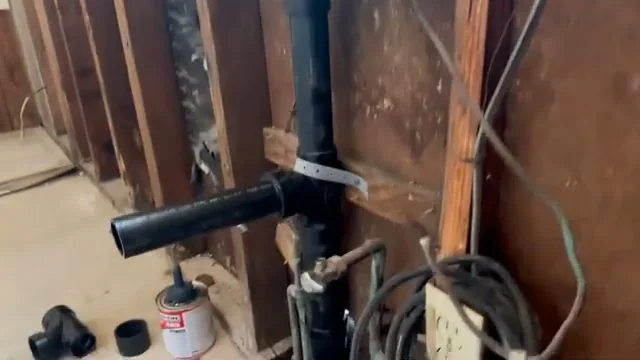 Vertical black drain pipe with a cleanout fitting inside a wall opened down to the studs.
