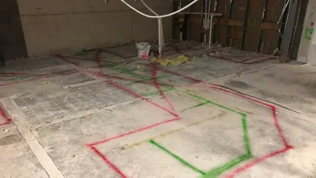 Red and green spray paint lines marking buried utilities across a concrete floor with a wall behind.