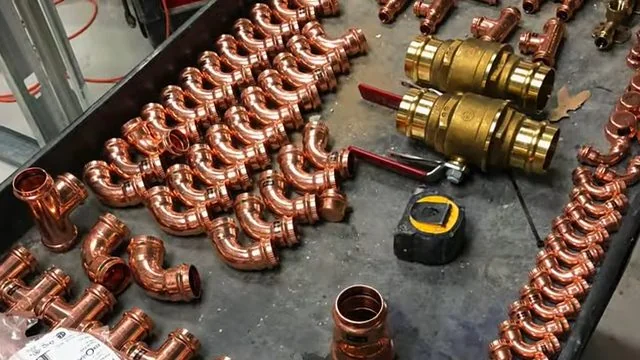 Copper elbows, tees and two brass ball valves laid out beside a tape measure on a work bench.