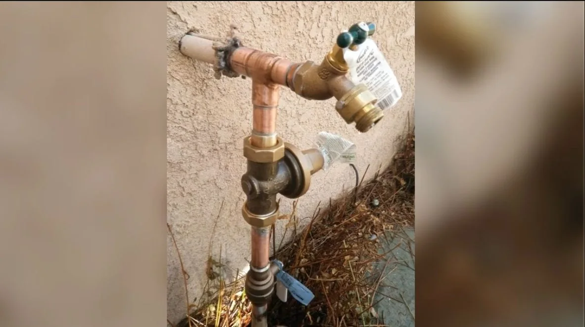 Copper pipe tee feeding a brass hose bib on a stucco wall, with dry leaves below.