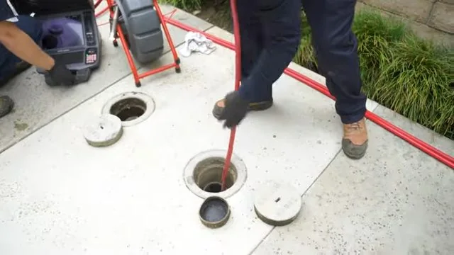Crew member feeding a red cable into a cleanout beside a second capped cleanout on a concrete walkway.
