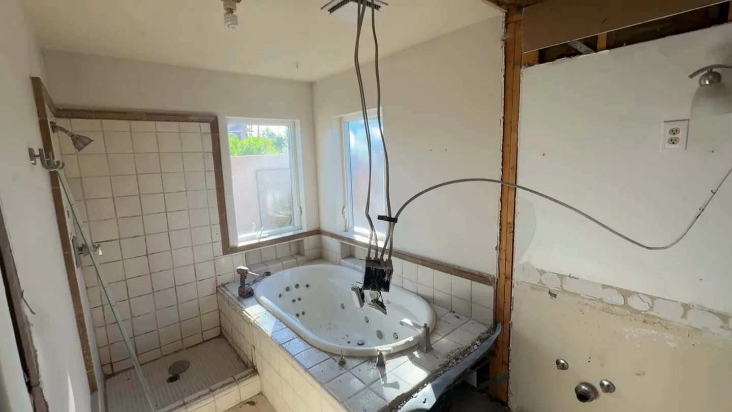 Demolished bathroom with a whirlpool tub, tiled shower wall and a bare floor.