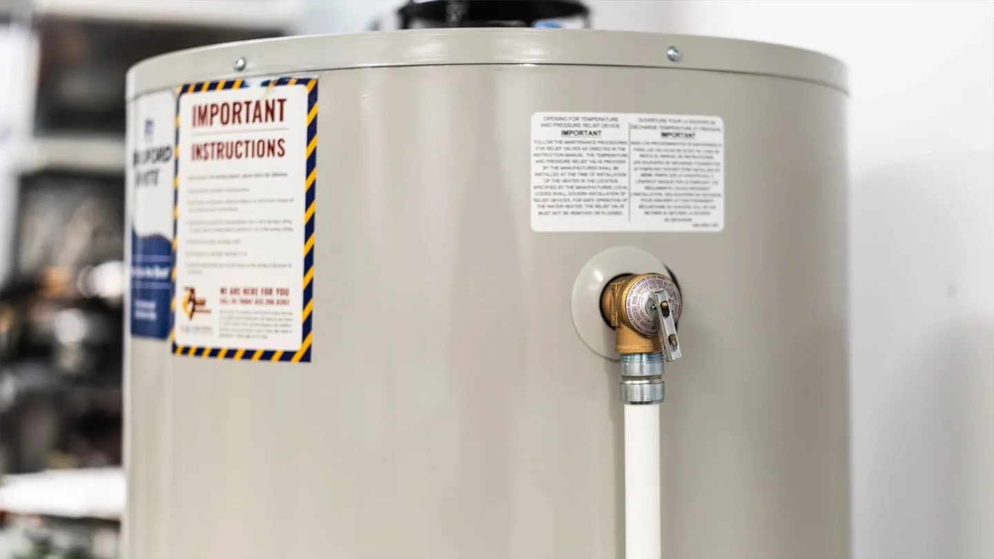 Electric water heater with a warning label and a valve with a short discharge pipe on its side.