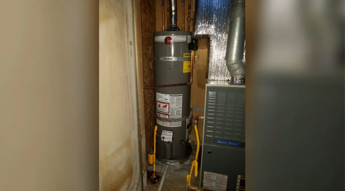 Gas water heater standing in a narrow framed closet, with ductwork nearby.
