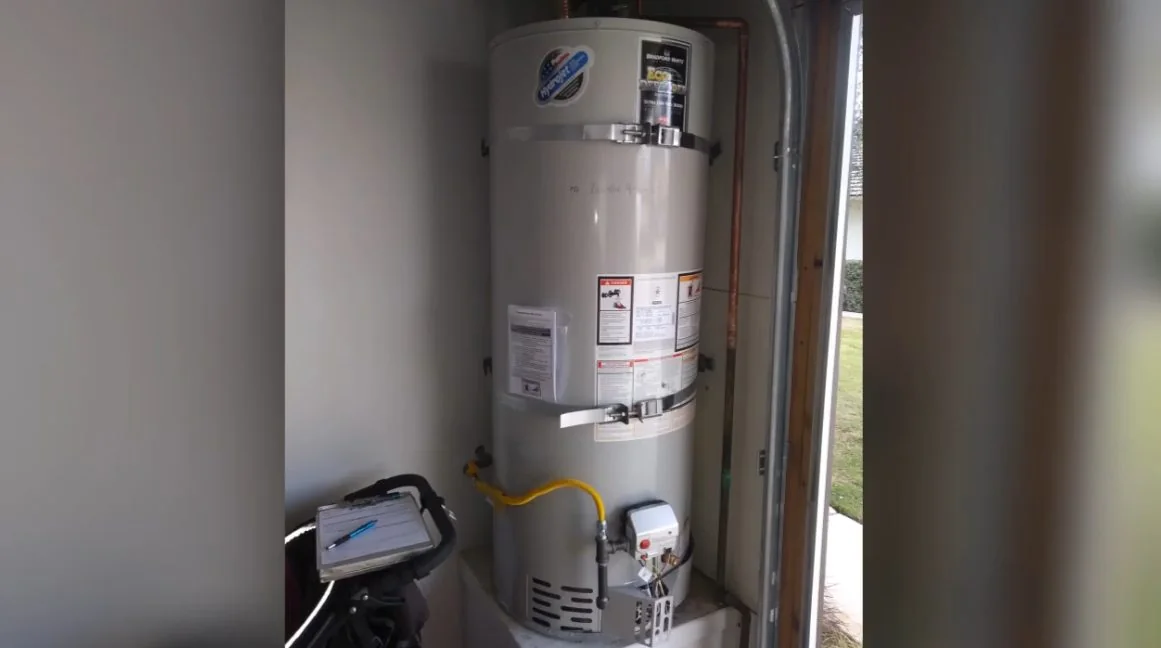 Gas tank water heater standing in a garage corner with a flue above and piping at its side.