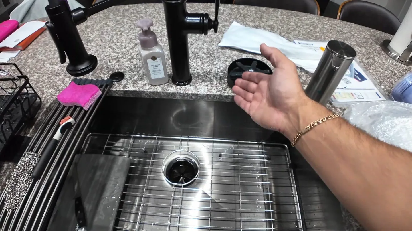 Hand resting at the strainer of a stainless kitchen sink as water runs in.
