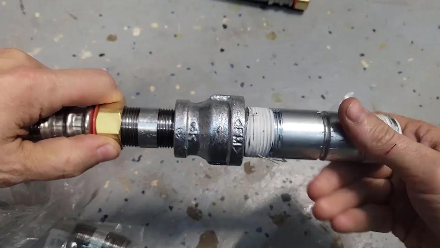Two hands screwing a threaded metal fitting onto a pipe on a worktable.
