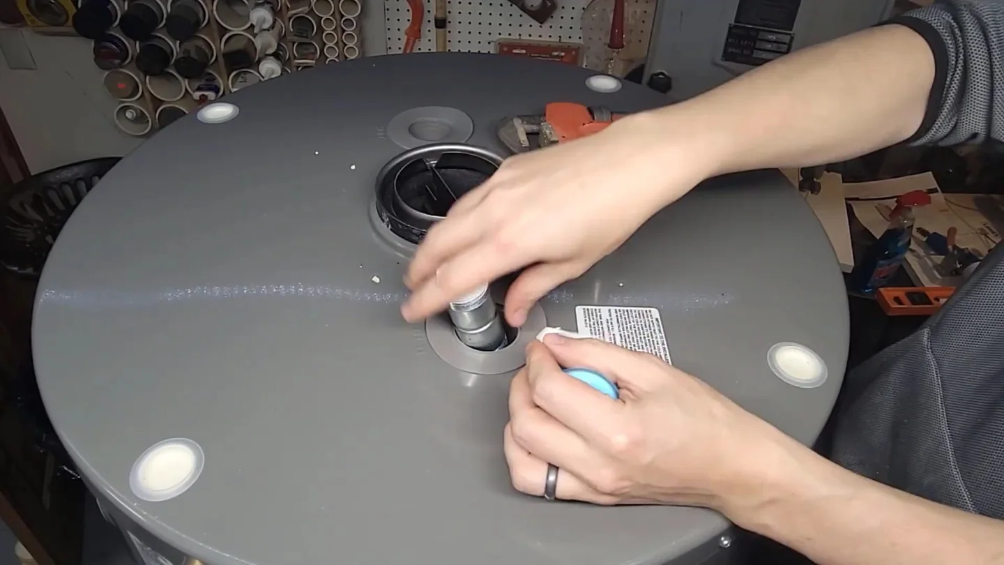Pair of hands at the top of a round gray tank, reaching toward a fitting and a label.