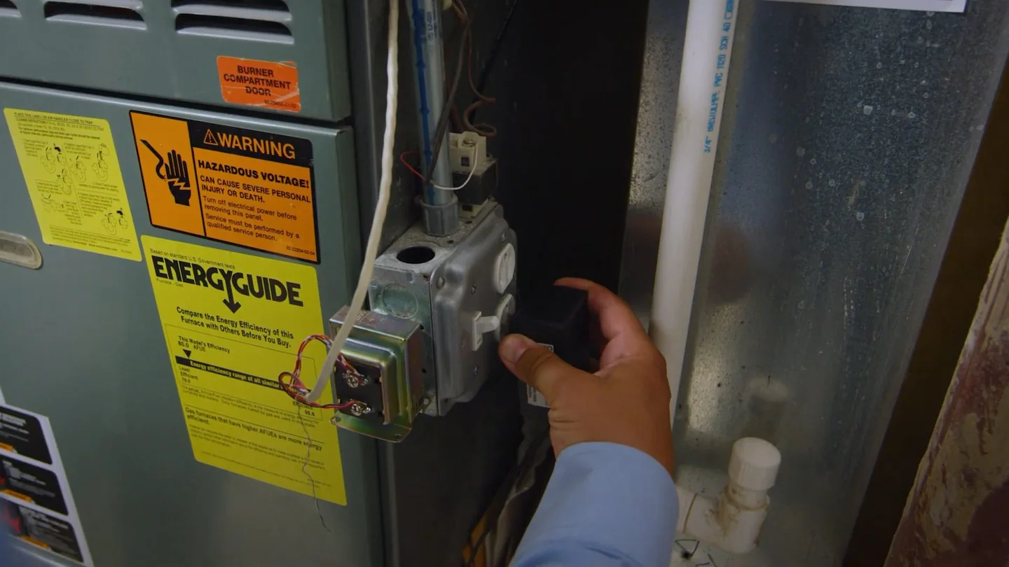 Hand on the control of a gas heater with yellow warning labels on the cabinet.