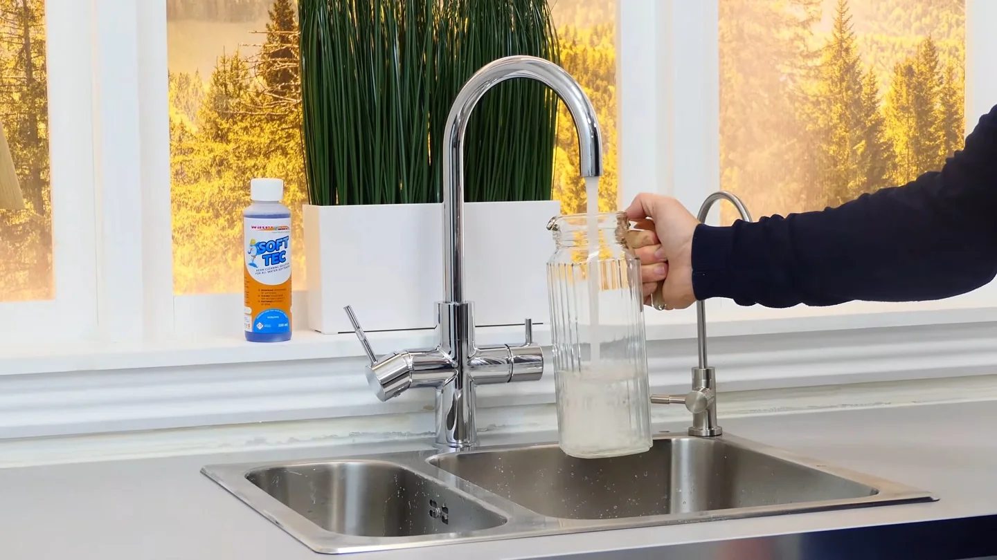 Tall chrome kitchen faucet running water over a double stainless sink beside a window.