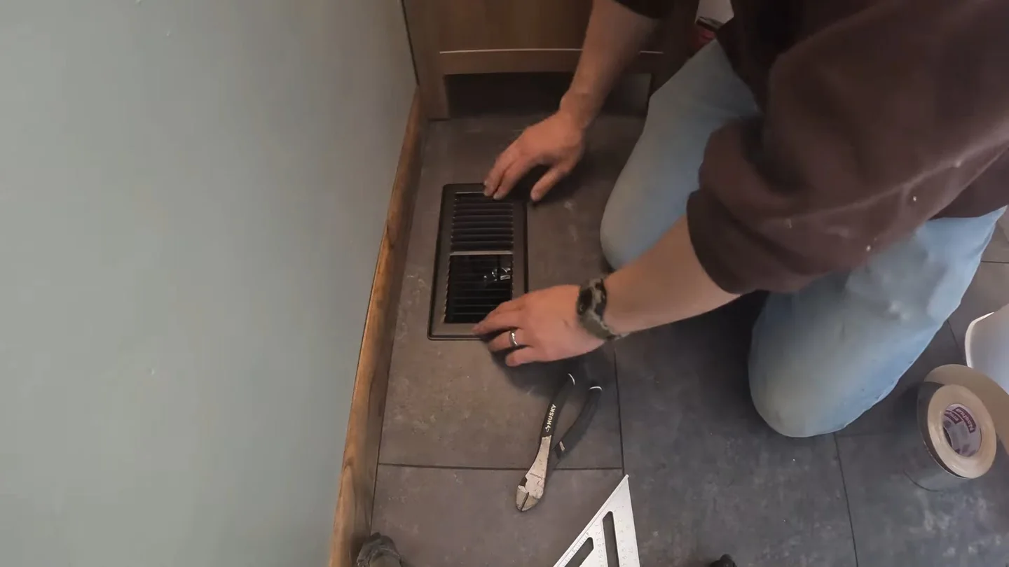 Man kneeling on a tiled floor with a wrench beside a floor drain cover.