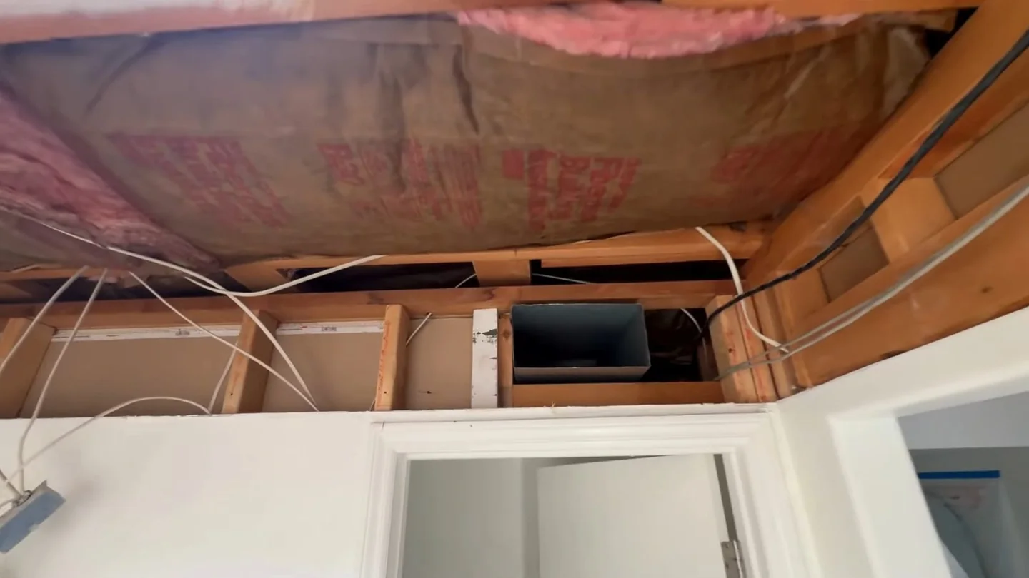 Opened ceiling above a doorway showing pink insulation, wiring and a framed access panel.