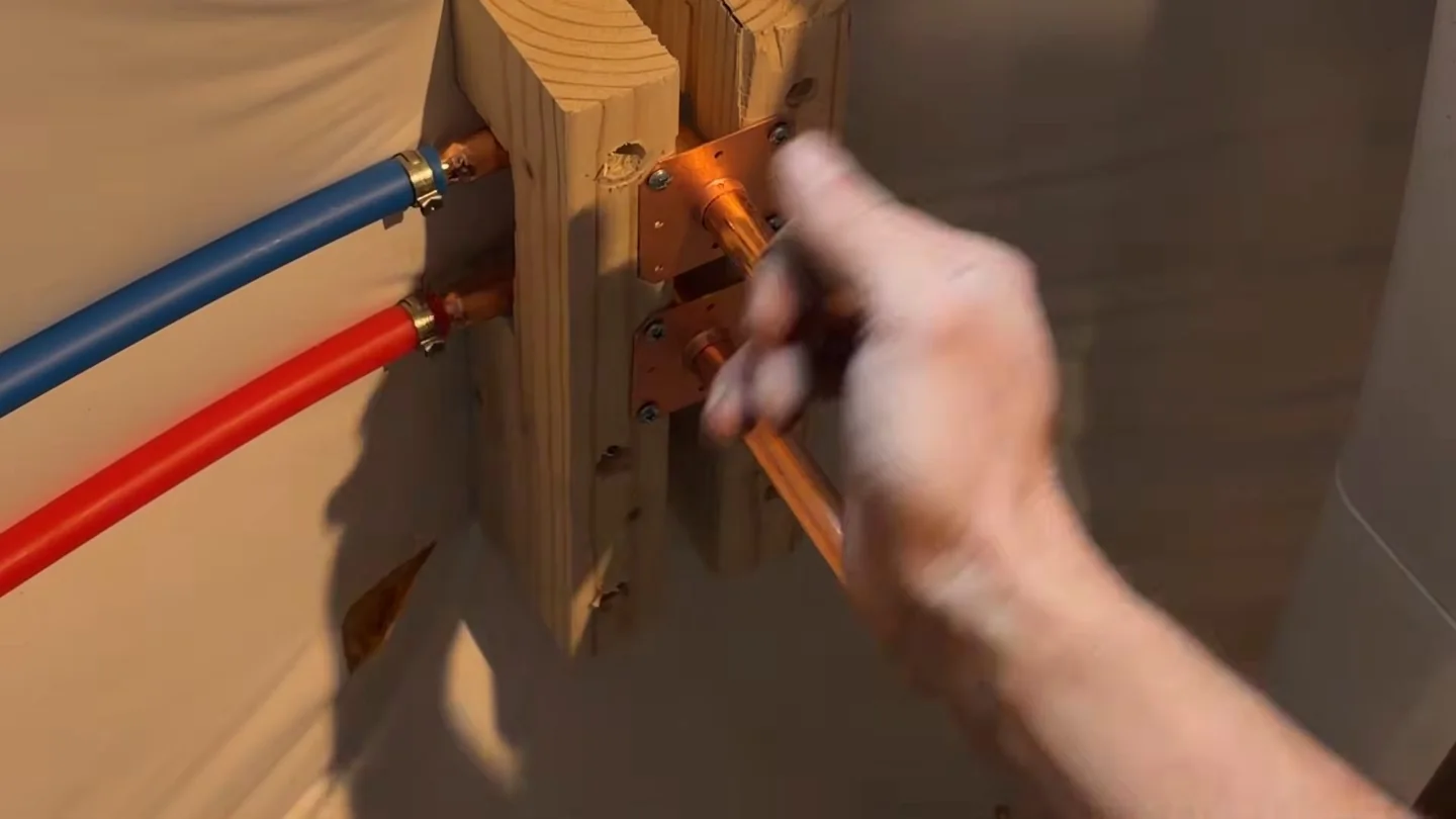 Hand adjusting red and blue PEX supply lines fixed to a wooden mounting block inside a wall.