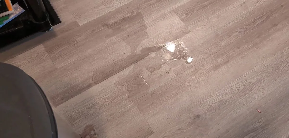 One drop of water on a gray plank floor, in close view.