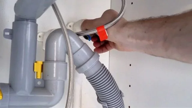 Hand holding a gray supply line near the shutoff valves and trap under a bathroom sink.