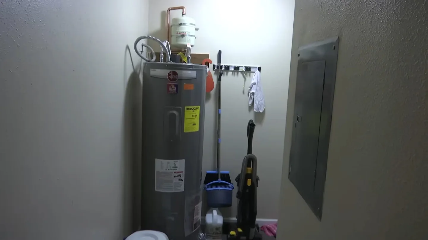 Tall tank water heater with piping against the wall of a utility closet.