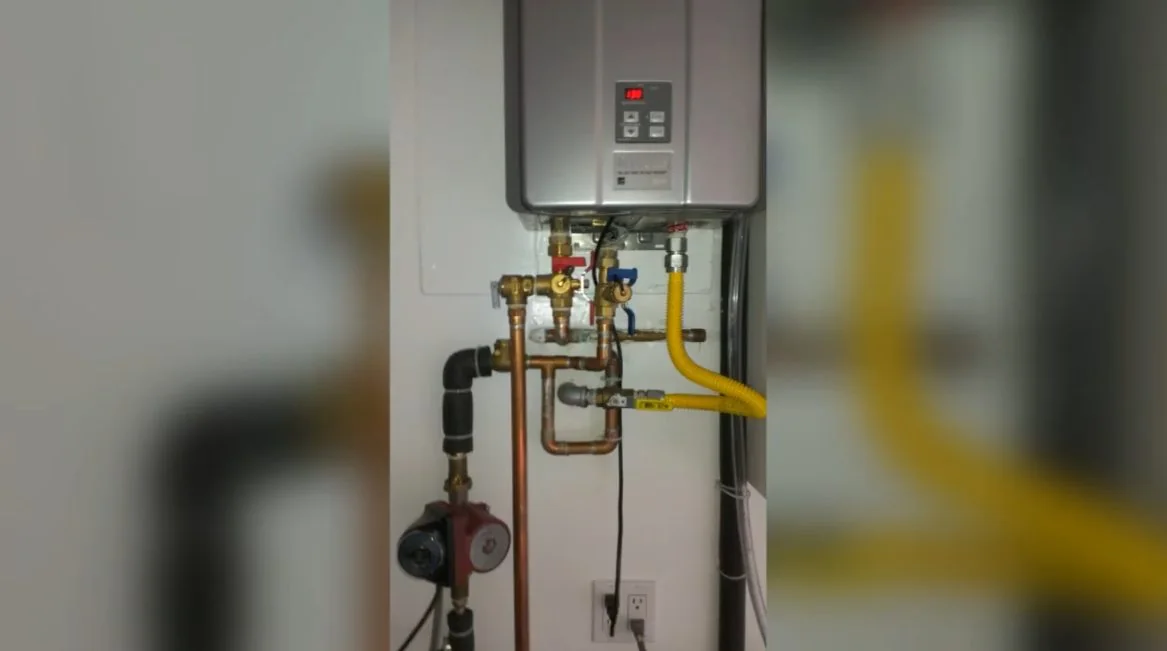 Tankless water heater on a wall with a yellow gas line and copper valves beneath it.