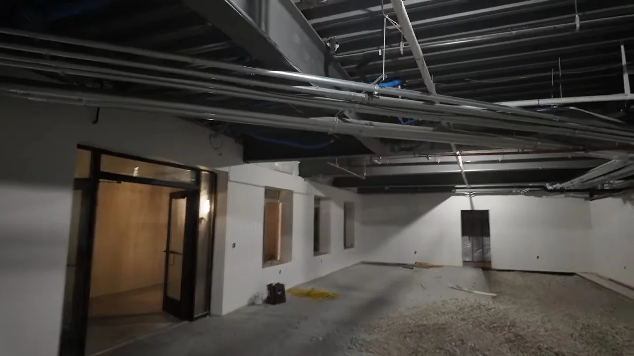 Unfinished commercial interior with exposed ceiling pipes and a bare concrete floor.