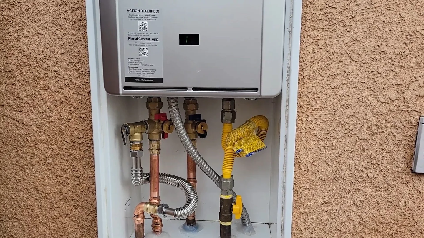 Wall-mounted tankless water heater in an open cabinet on a stucco wall with valves and gas line below.
