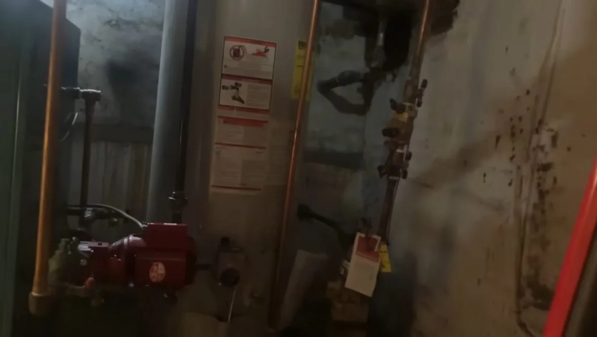 Water heater with a red-handled valve and copper lines in a dim utility room.