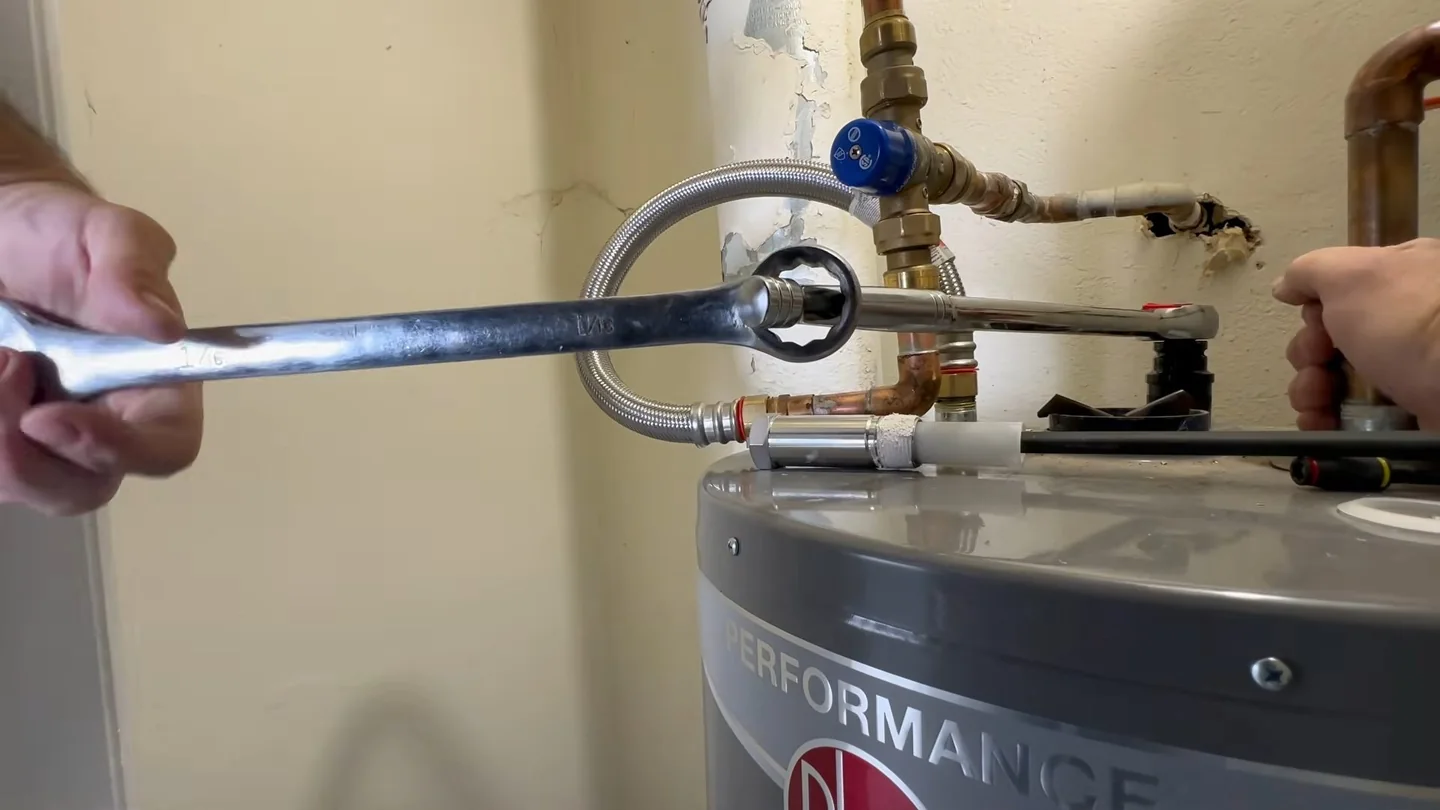 Wrench gripping a fitting at the top of a water heater with a hand holding the line steady.