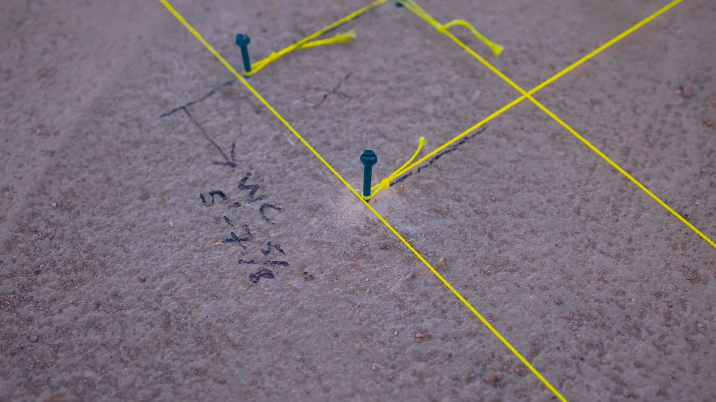 Yellow string lines and handwritten notes marking spots on a gray carpeted floor.
